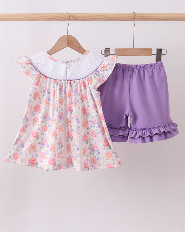 Floral top and purple shorts on hangers against a white background