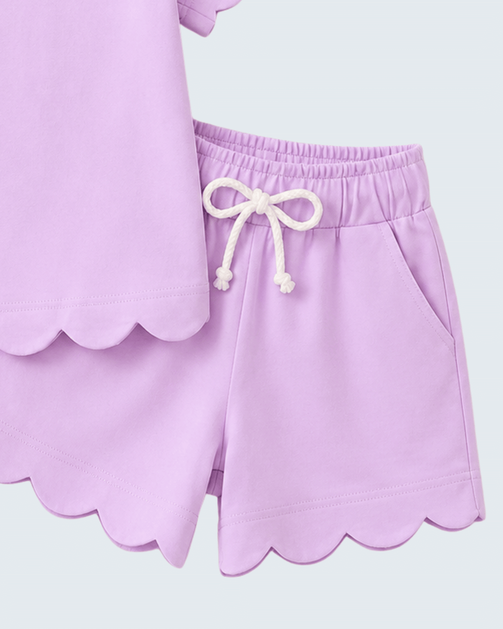 Close-up of a lilac outfit with scalloped hem and drawstring waistband on a light gray background.