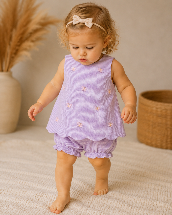 Young child wearing a purple outfit with floral patterns on a neutral background
