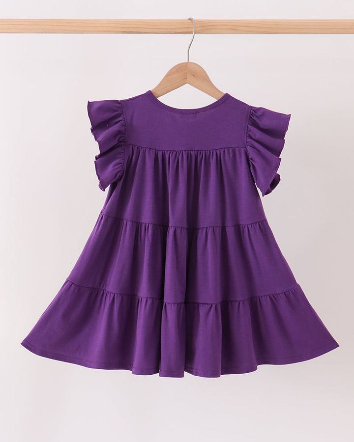 A purple tiered dress with ruffled cap sleeves hanging on a wooden hanger from a light wood rod against a plain off-white background.