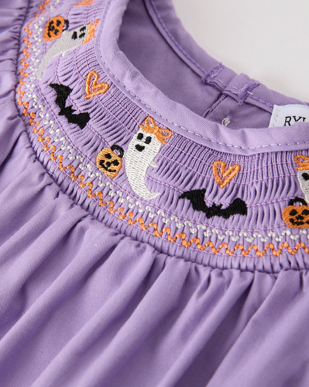 Close-up of lavender smocked yoke with orange-trimmed Halloween cat and pumpkin embroidery