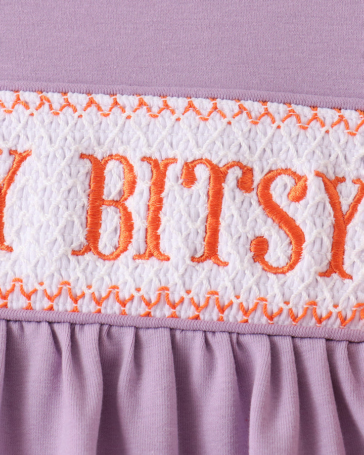 Lilac top with white smocked yoke and orange embroidered “Itsy Bitsy” text