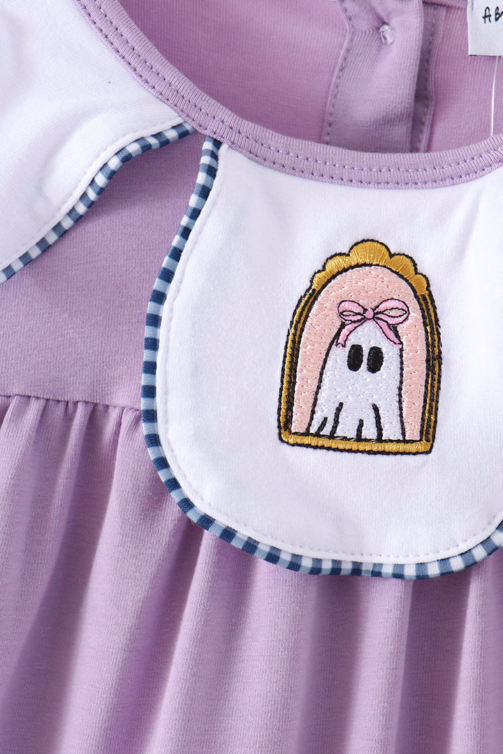 Close-up of a baby dress in light purple with a white bib featuring a ghost patch and blue-and-white gingham trim.