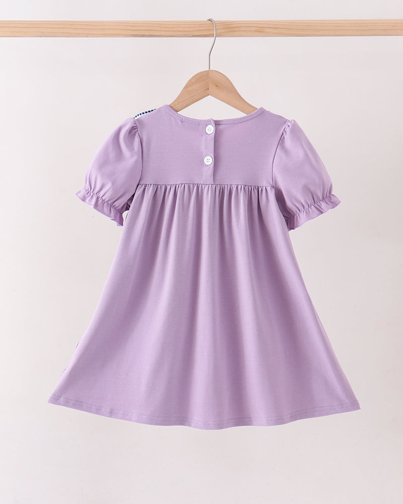 A light purple short-sleeve baby dress with puff sleeves and a gathered waist, hanging on a wooden hanger against a plain off-white background.