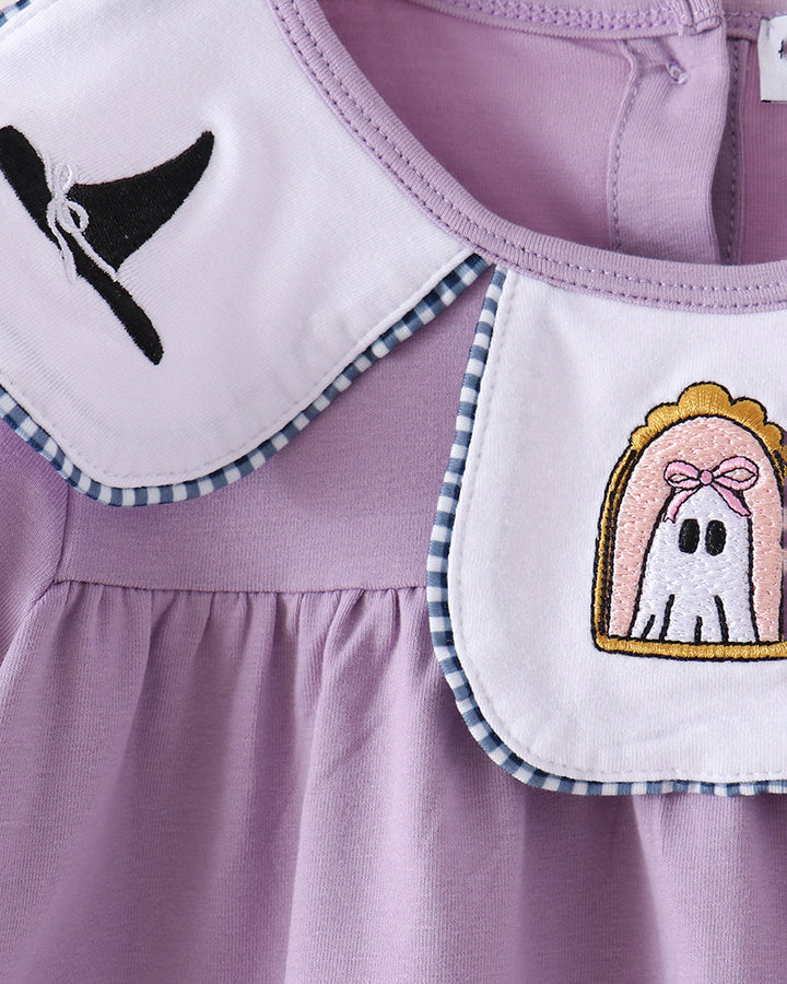 Close-up of a lavender baby dress with a white Peter Pan collar featuring a black witch hat embroidery on one side and a ghost patch on the other, with blue-and-white gingham trim.