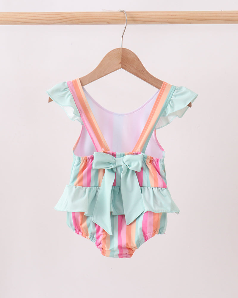 Colorful swimsuit with ruffles on a hanger against a light pink background