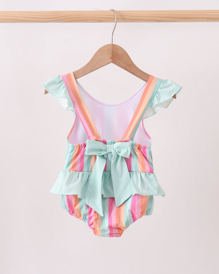 Colorful swimsuit with ruffles on a hanger against a light pink background