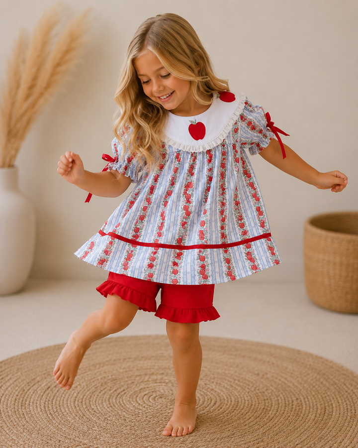 Young girl wearing a dress with red and white pattern, standing on a woven mat.