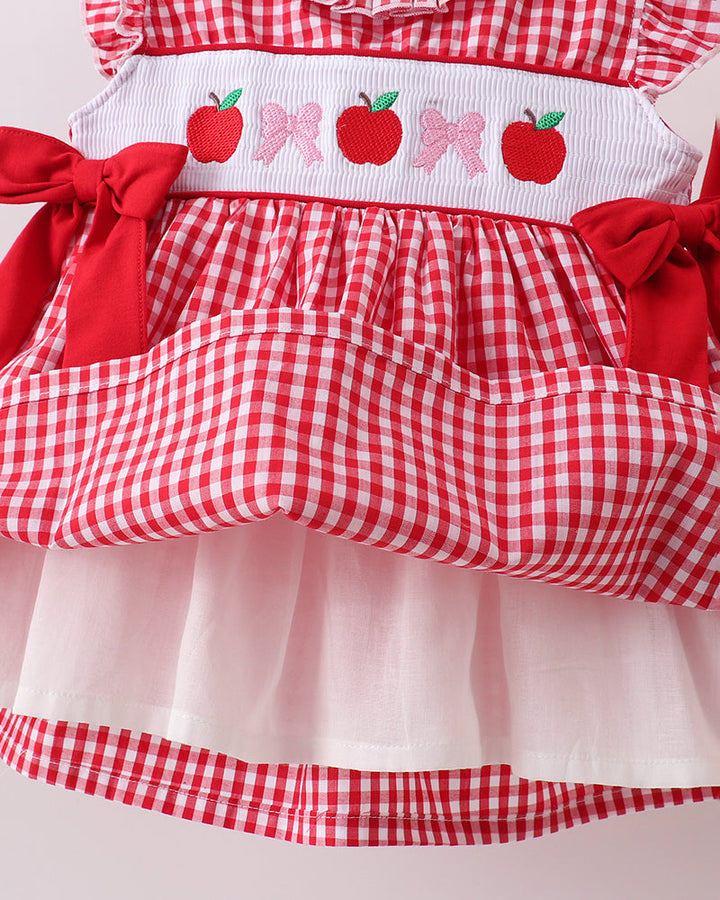 Red and white checkered dress with apple and bow pattern on a plain background