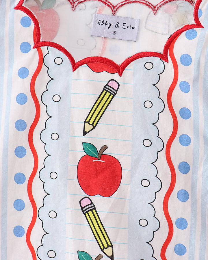Close-up of neckline with apple and pencil graphics on white dress, scalloped red trim