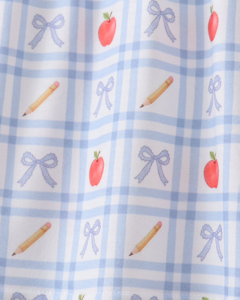 Close-up of blue gingham top with scattered apple, bow and candy stick motifs