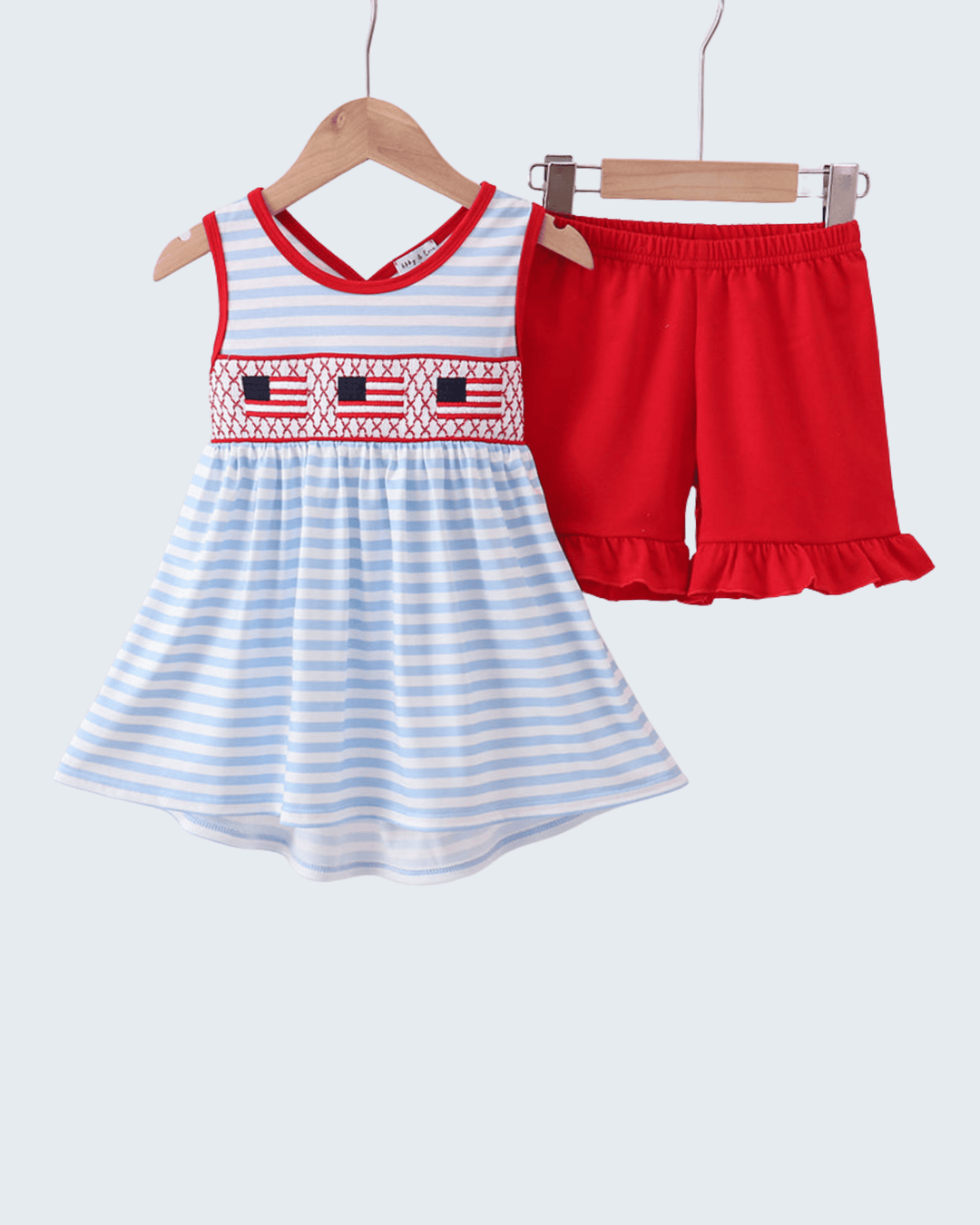 Children's dress with red and white accents and red shorts on hangers against a white background