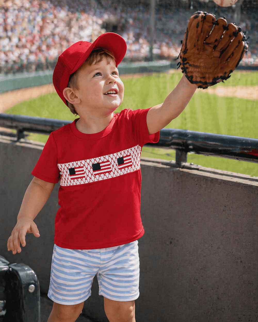 Child in a red shirt and cap with a baseball glove at a stadium