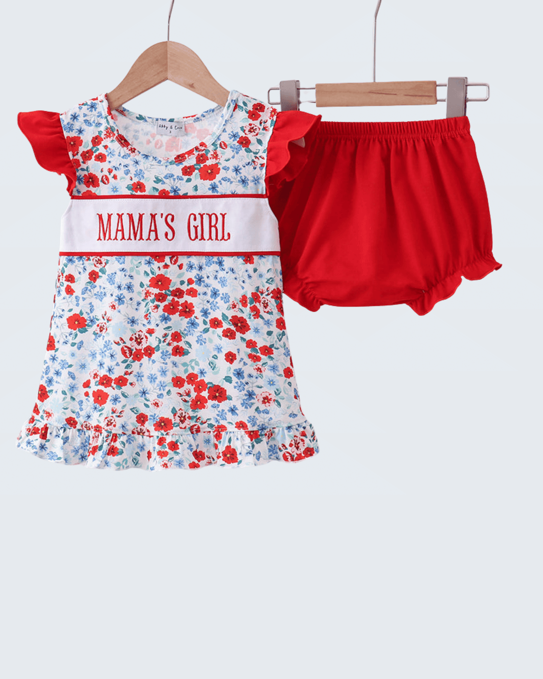 Children's outfit with floral dress and red bloomers on hangers against a white background