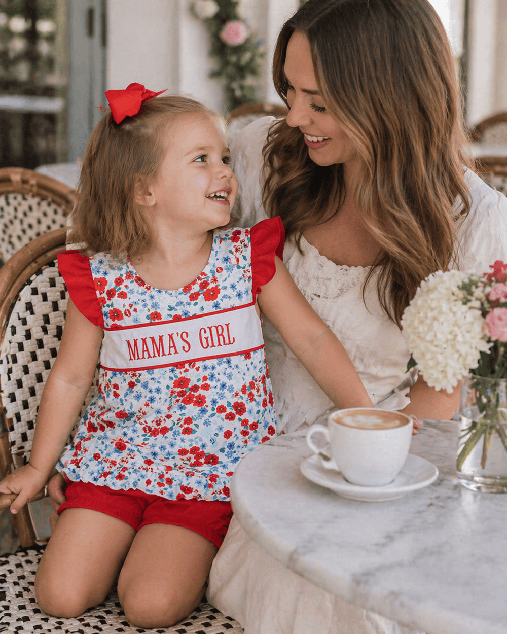Woman and young girl sitting at a table with a cup of coffee, smiling.