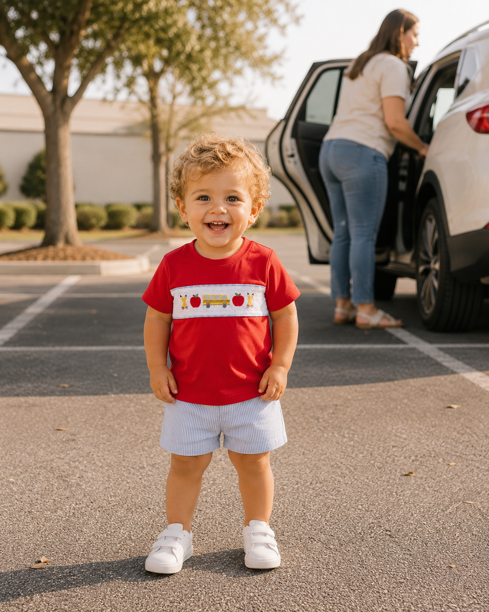 Child wearing red smocked T-shirt with white panel and school bus applique
