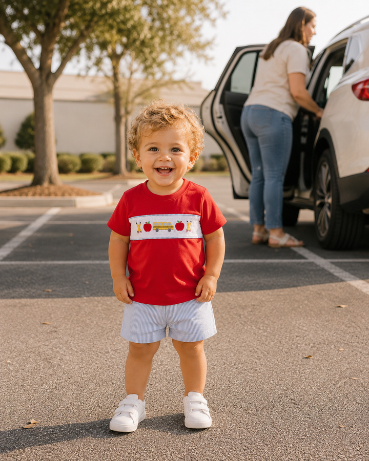 Child wearing red smocked T-shirt with white panel and school bus applique