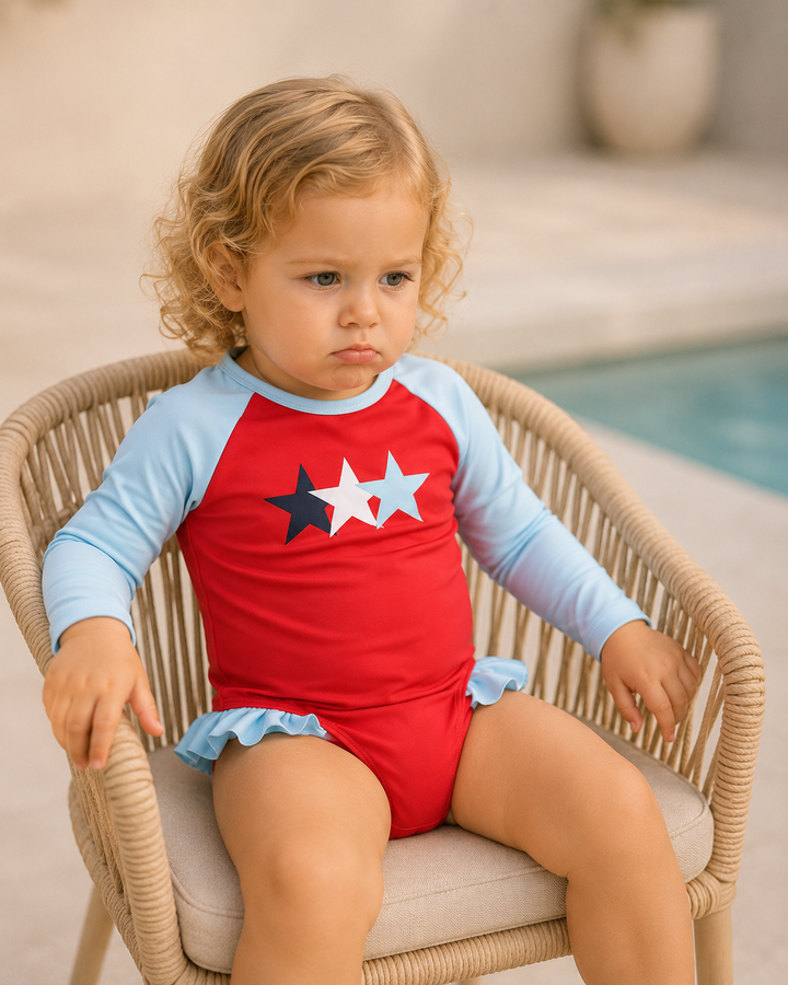 Child wearing a red and blue swimsuit with star design, sitting on a chair by a pool.