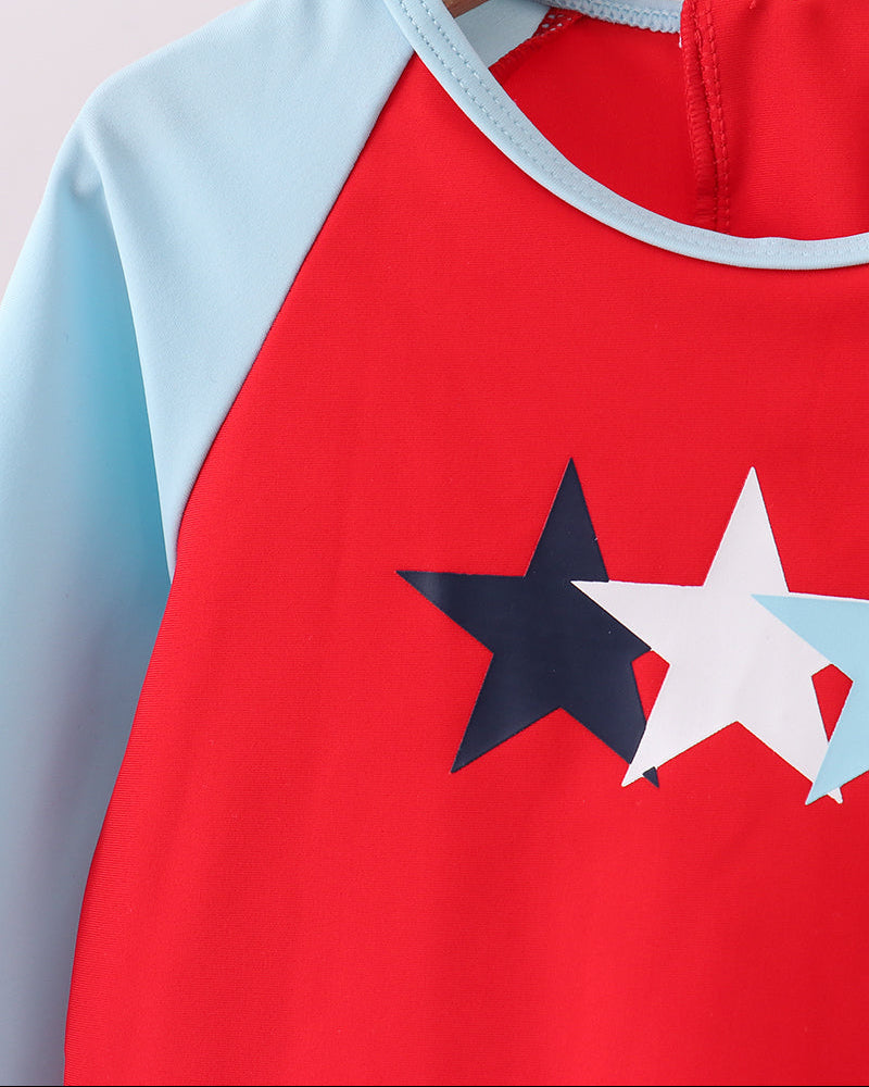 Red rashguard with blue sleeves and star designs on a hanger