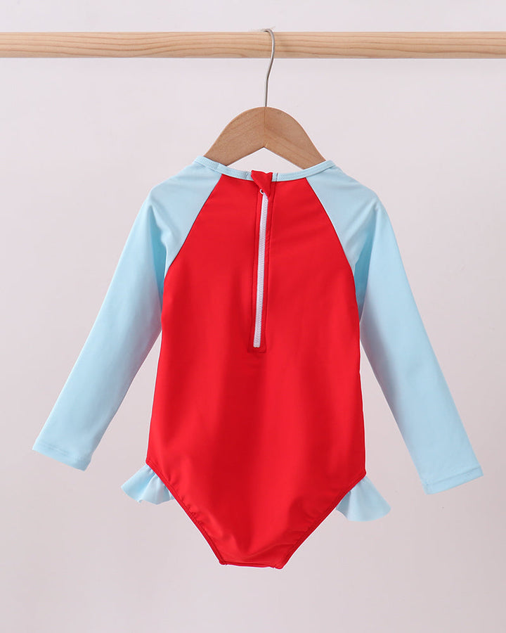 Red and light blue swimsuit on a wooden hanger against a beige background