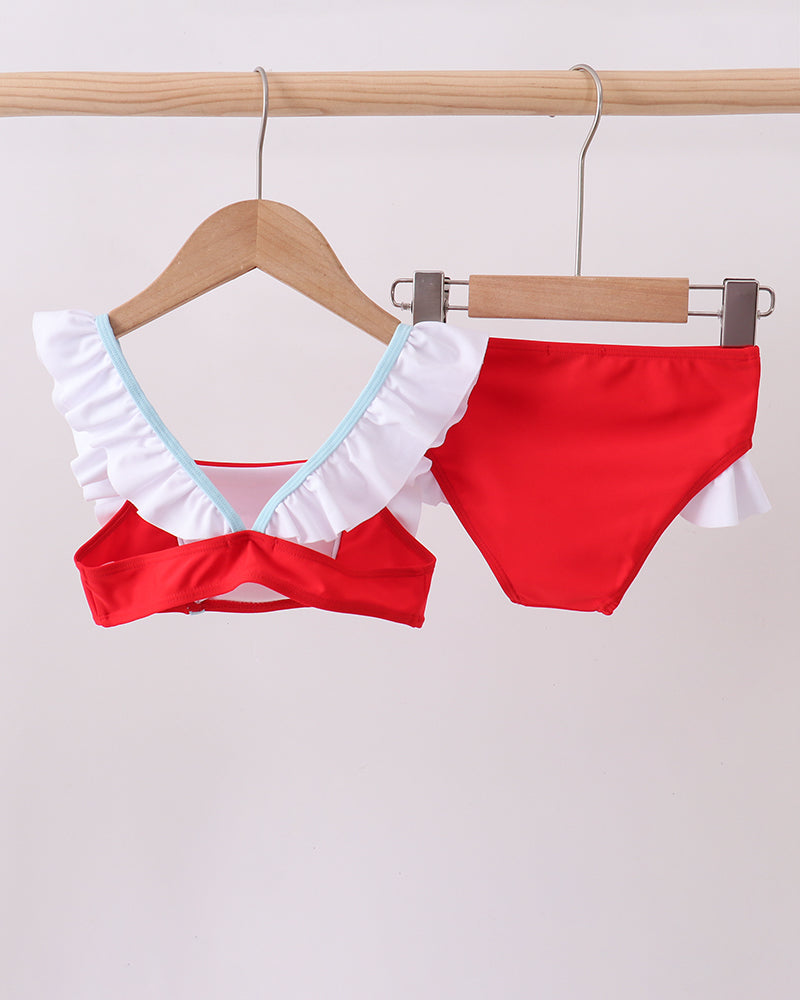 Red bikini with white ruffled details on a wooden hanger against a light gray background