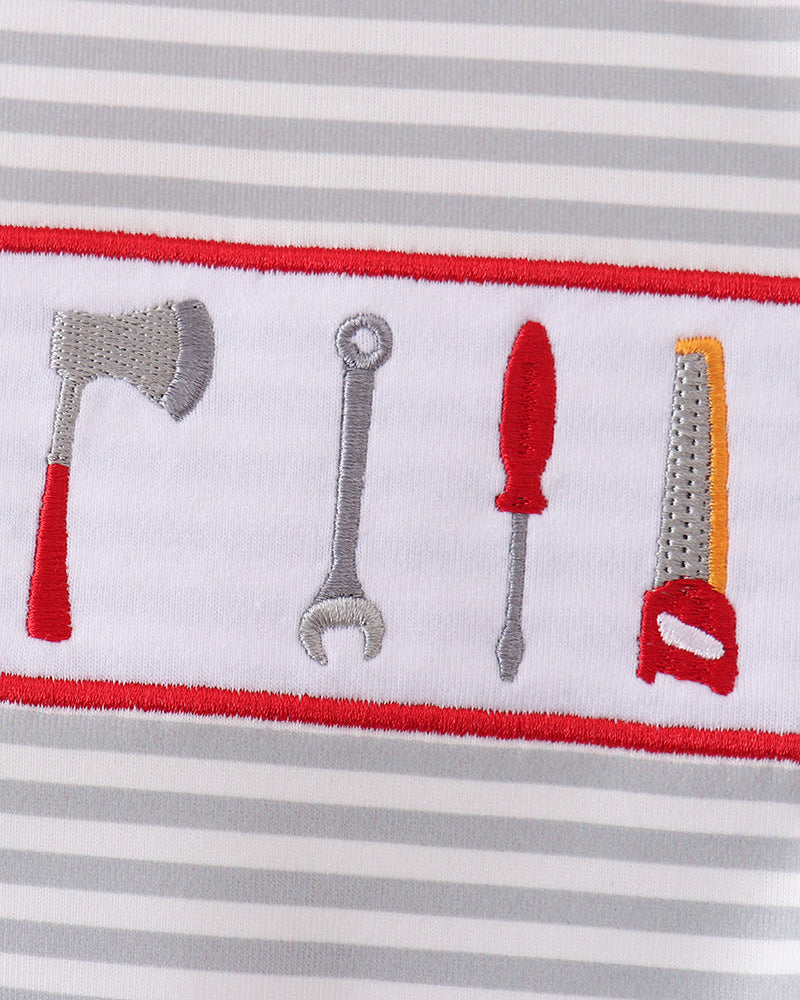 Close-up of a striped fabric with an embroidered horizontal band showing tool motifs: an axe, wrench, screwdriver, and saw, outlined in red.