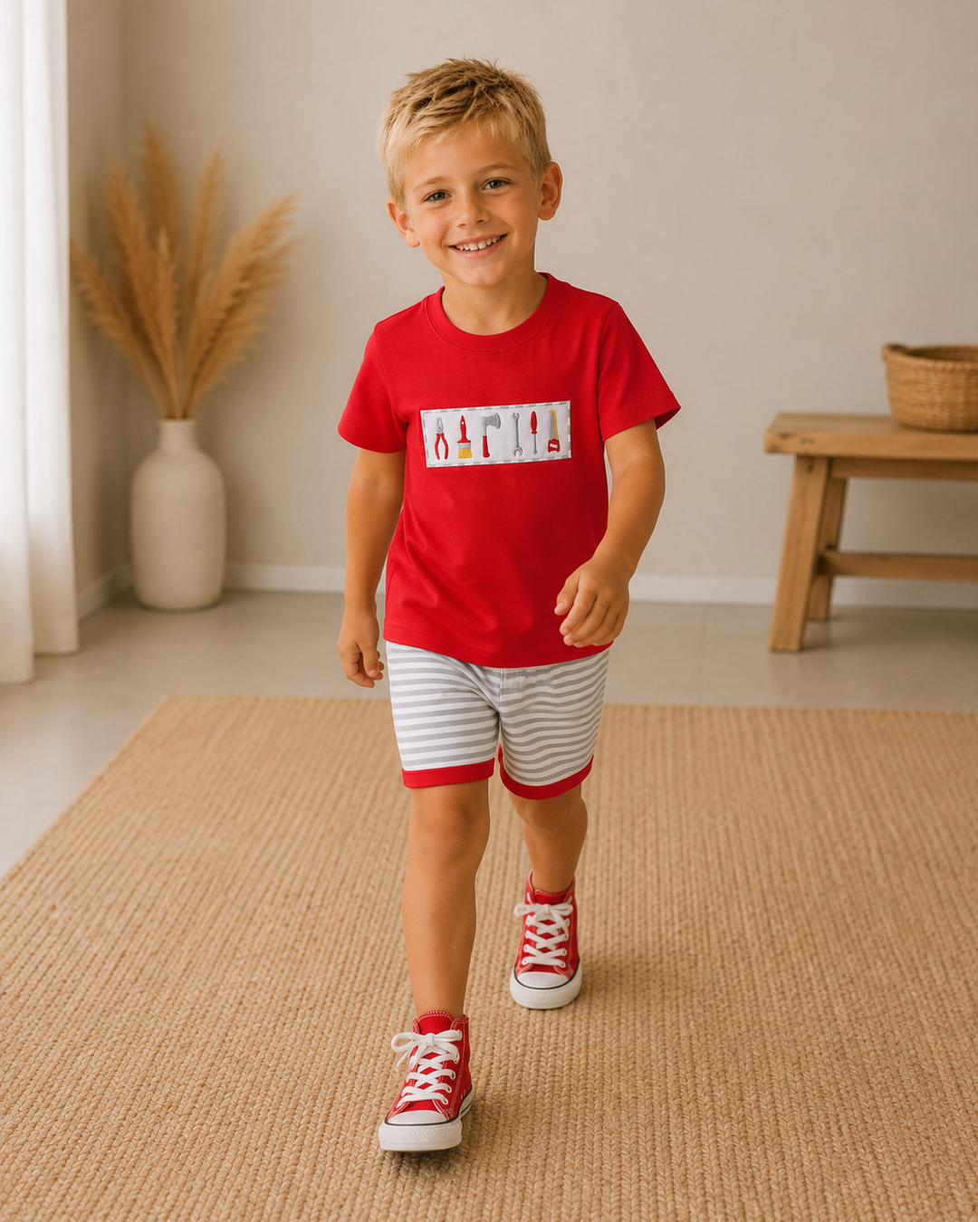 A young boy walking on a beige woven rug in a bright room, wearing a red crewneck t-shirt with a white graphic print and red-and-white striped shorts.