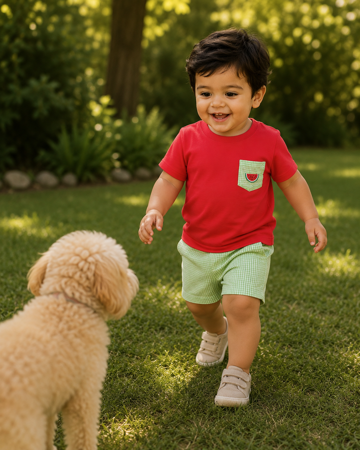 Child in a red shirt and green shorts running on grass with a dog