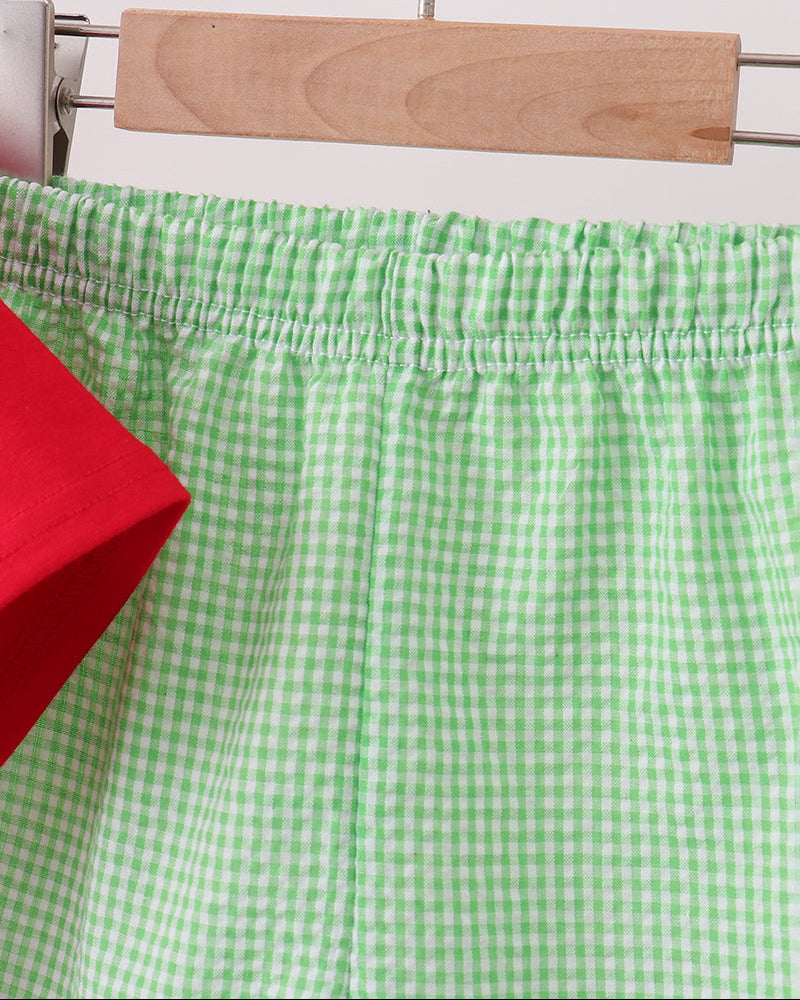 Green checkered pants on a hanger against a white tiled wall.