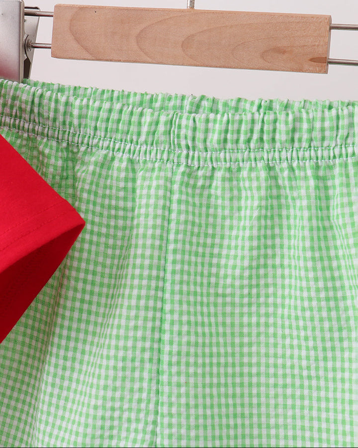 Green checkered pants on a hanger against a white tiled wall.