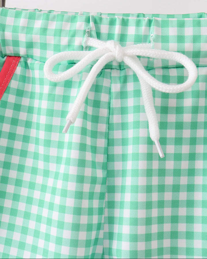 Green and white checkered shorts with a drawstring on a wooden hanger.