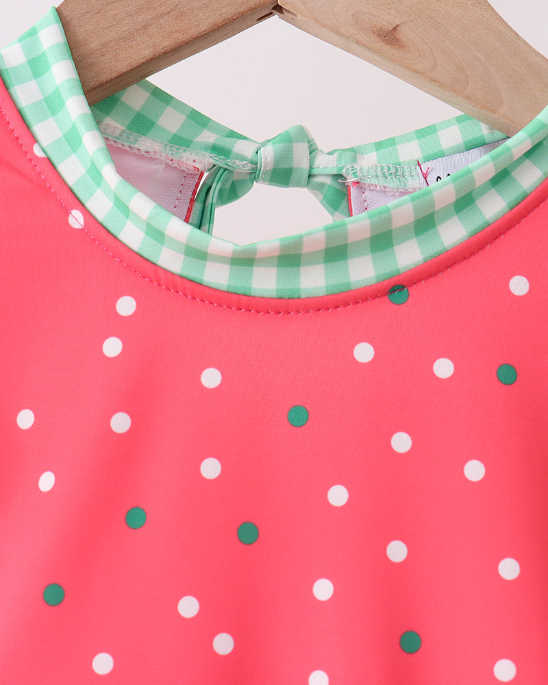 Swimsuit with white polka dots and green checkered collar on a wooden hanger.