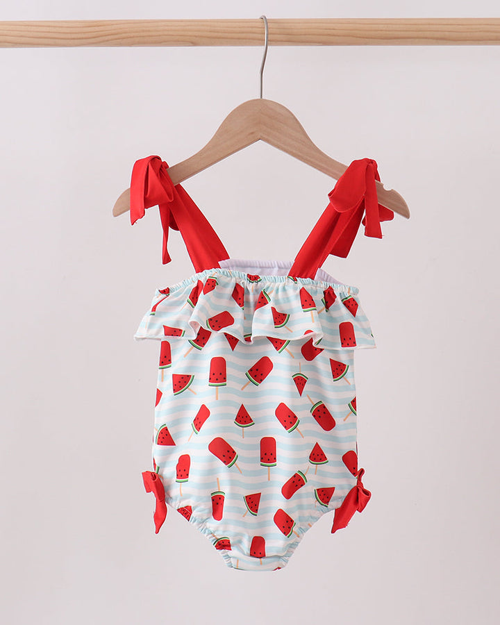 Swimsuit with watermelon pattern and red straps on a hanger against a light background