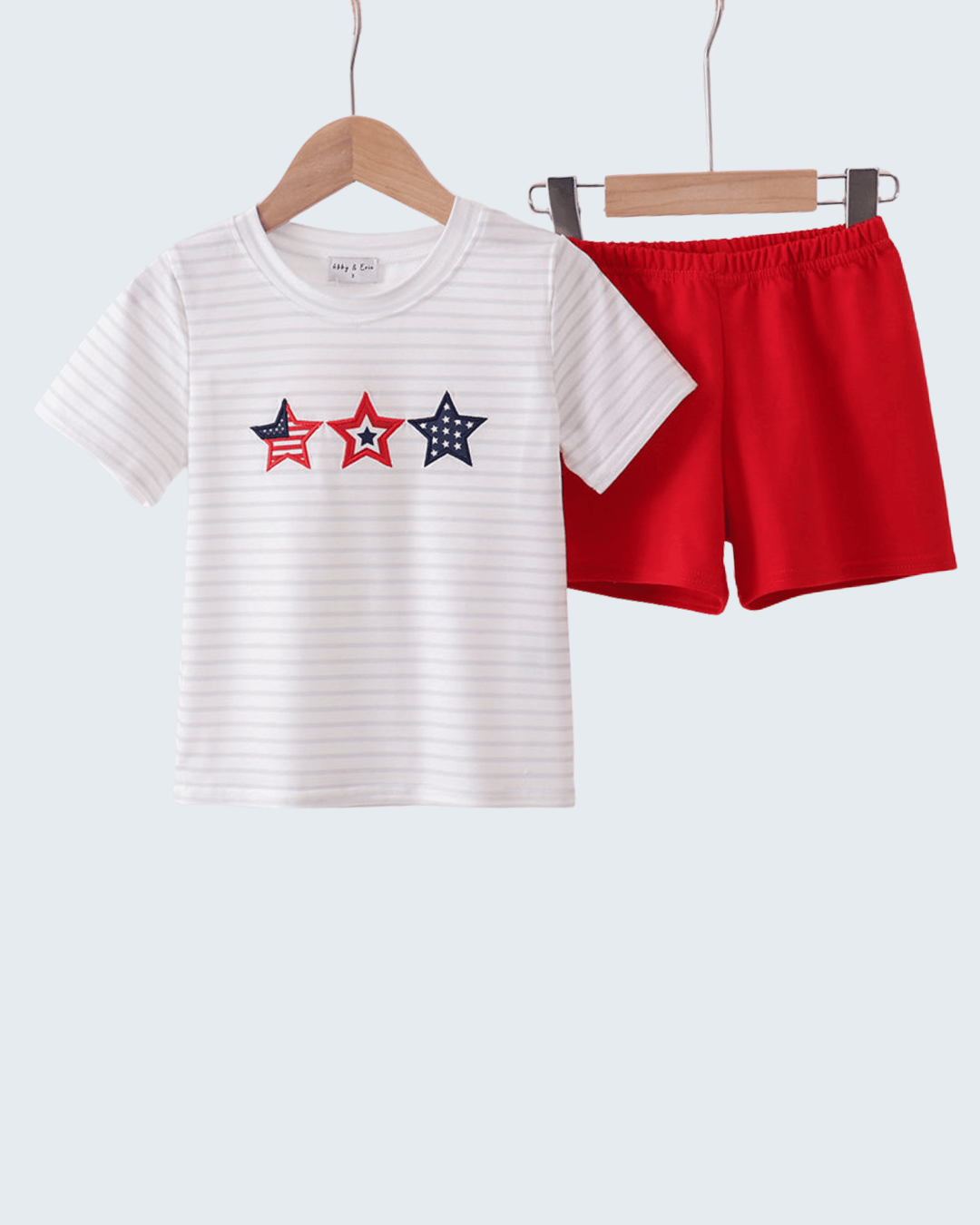 White t-shirt with red and blue star design and red shorts on hangers against a white background