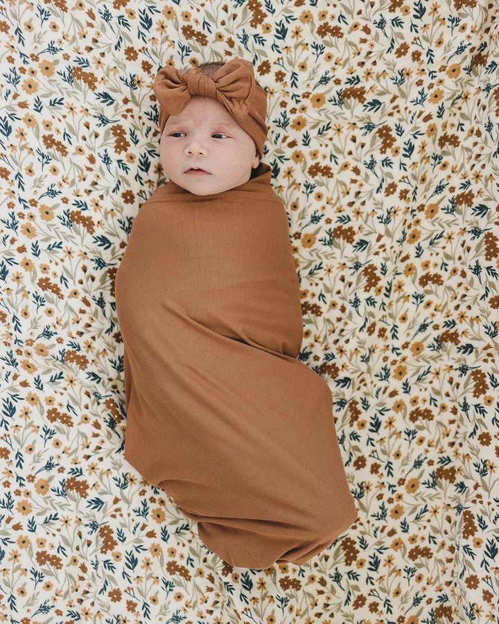Rust knotted head wrap with bow on a baby against floral bedding