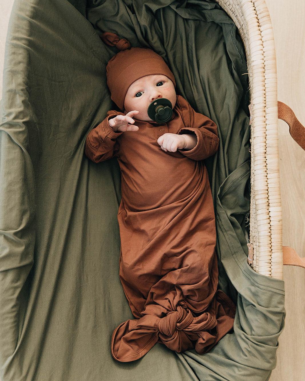 Baby in a brown outfit and hat lying in a green crib
