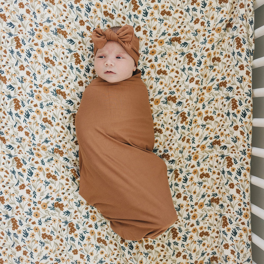 Baby wearing rust-brown swaddle and knotted head wrap