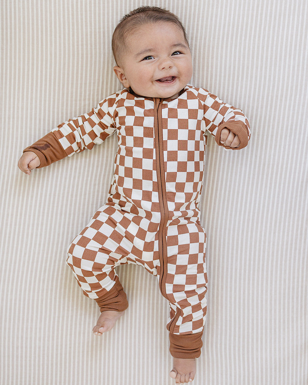 Baby wearing a brown and white checkered onesie on a neutral background