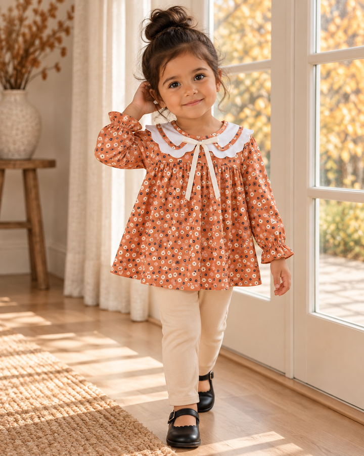 Young girl wearing rust floral dress with white Peter Pan collar and beige pants