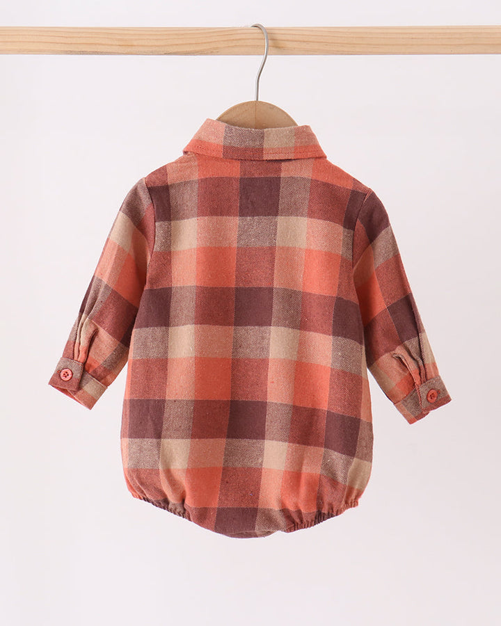 A baby long-sleeve plaid romper in a warm autumn color palette, hanging on a wooden hanger from a wooden clothes rack against a plain white background.