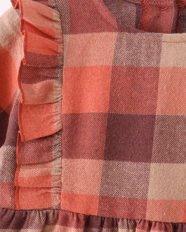 Close-up of a plaid dress in warm autumn tones, featuring a large ruffle trim on the left side with a check pattern in orange, rust, brown, and beige.
