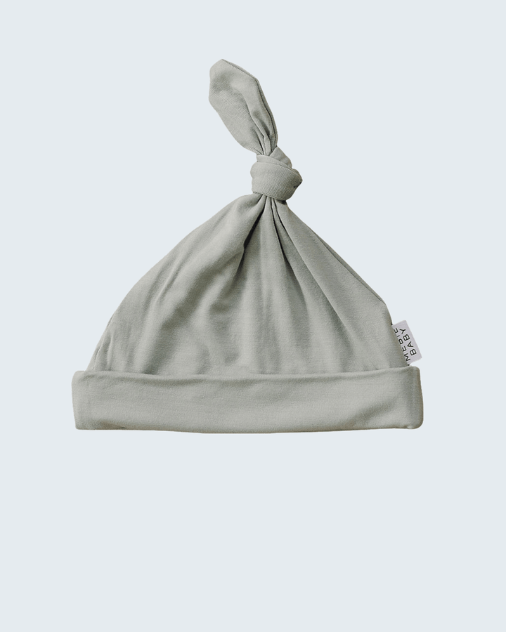 Sage baby hat with a knot on a light gray background