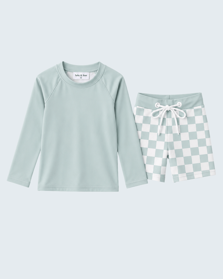 Swim set with mint green long-sleeve top and checkered shorts on a light blue background.