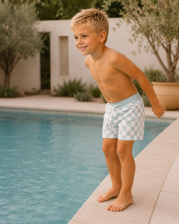Young boy in checkered swim shorts standing by a pool