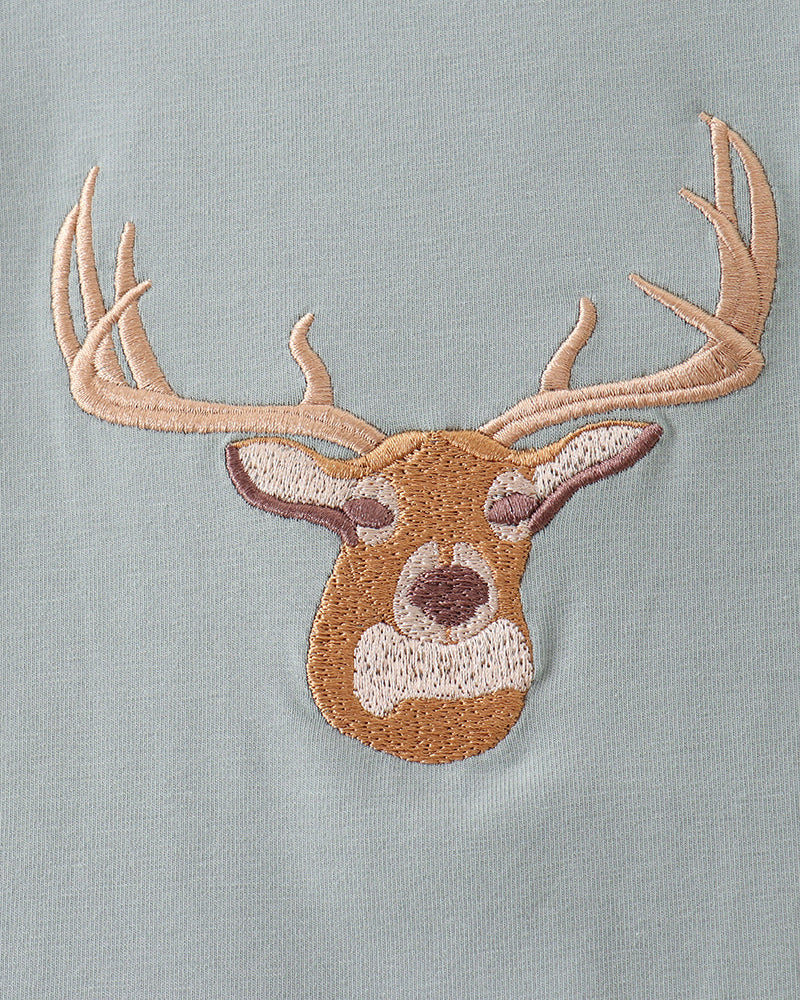 A close-up of a light sage green fabric featuring an embroidered deer head with tan antlers and a brown and cream face.