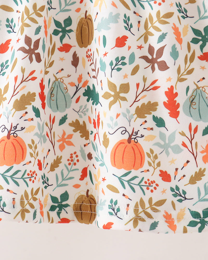 A close-up of a white fabric with a colorful autumn pattern featuring pumpkins, leaves, and berries in orange, green, brown, and red.