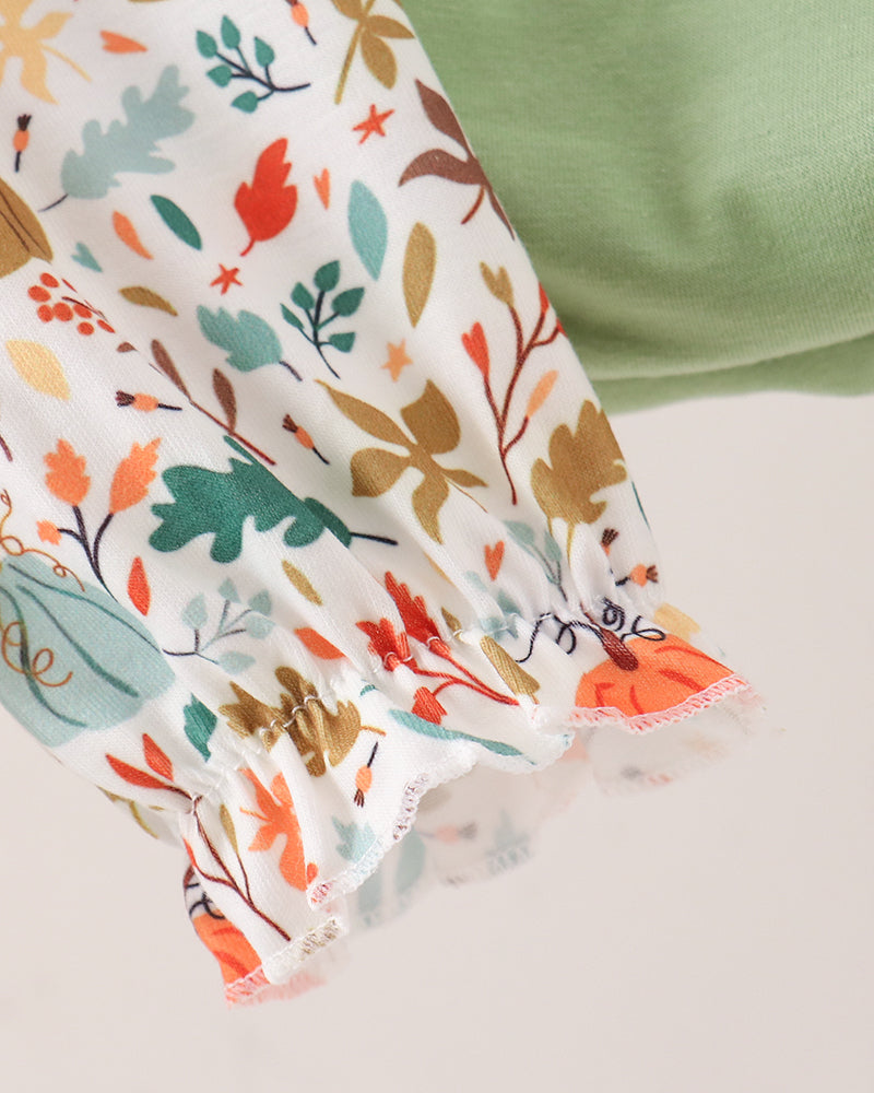 A close-up of a white fabric sleeve or garment section with a colorful autumn leaf and pumpkin print, featuring ruffled edges and a soft green fabric section in the background.