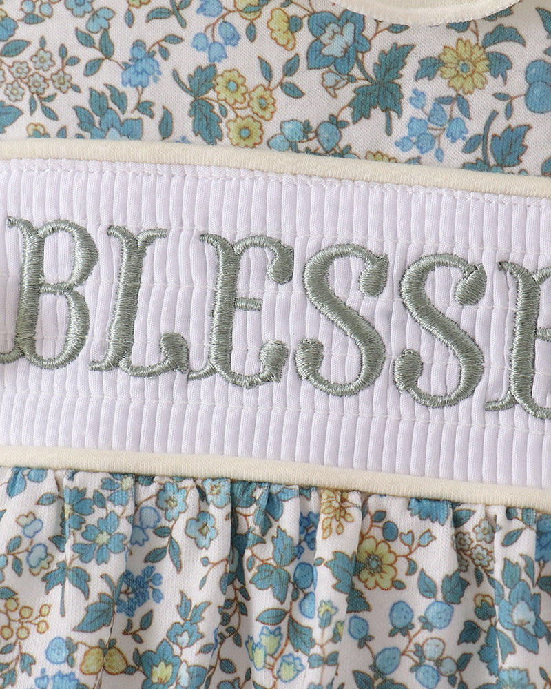 "Blessed" embroidered on white smocked band of blue floral bubble romper