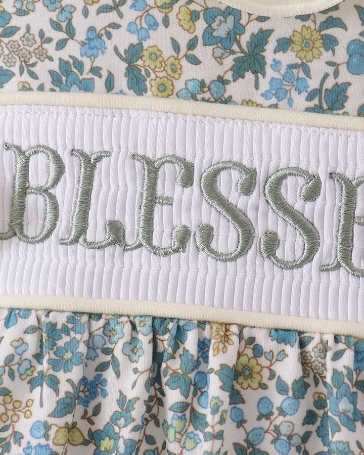 "Blessed" embroidered on white smocked band of blue floral bubble romper