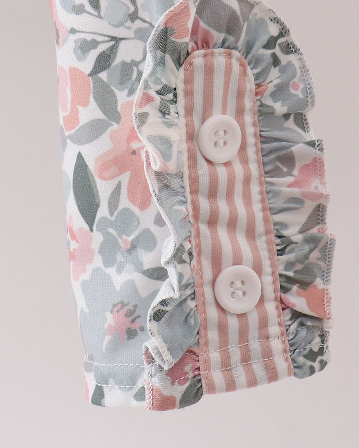 Close-up of a ruffled sleeve or garment detail with a pink, gray, and white floral print on one side and a pink-and-white striped fabric panel with two white buttons on the other, set against a light neutral background.